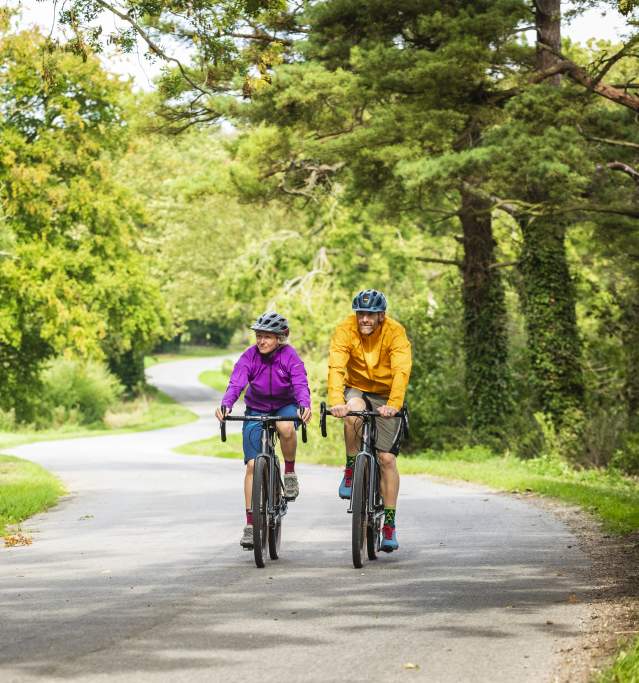 Two people cycling through a forest on a path
