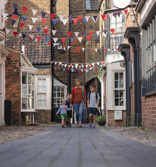 a family walking along a side street with bunting hanging from the buildings