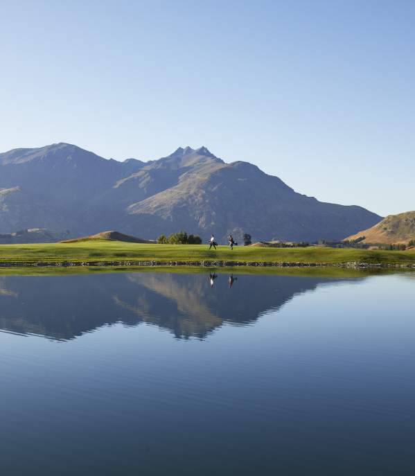 Wide shot of a golf course with lake reflecting mountains