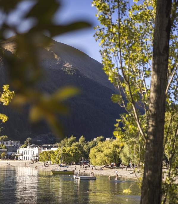 Looking through green trees to big lake, boats, people and buildings