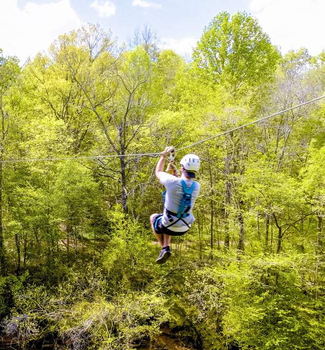 Person with helmet ziplinging through the trees