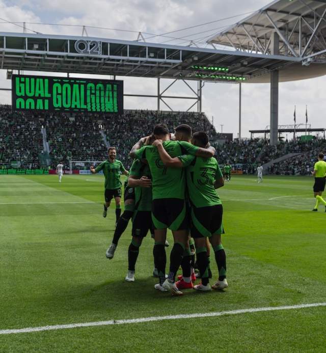 Image of some Austin FC players huddling on the field at Q2 Stadium during a game.