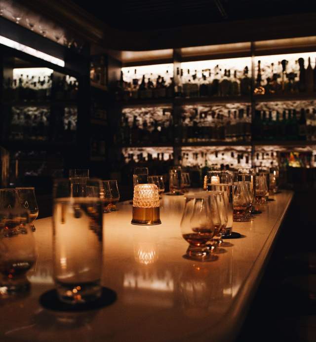 Moody, dimly lit bar lined with cocktail glasses.