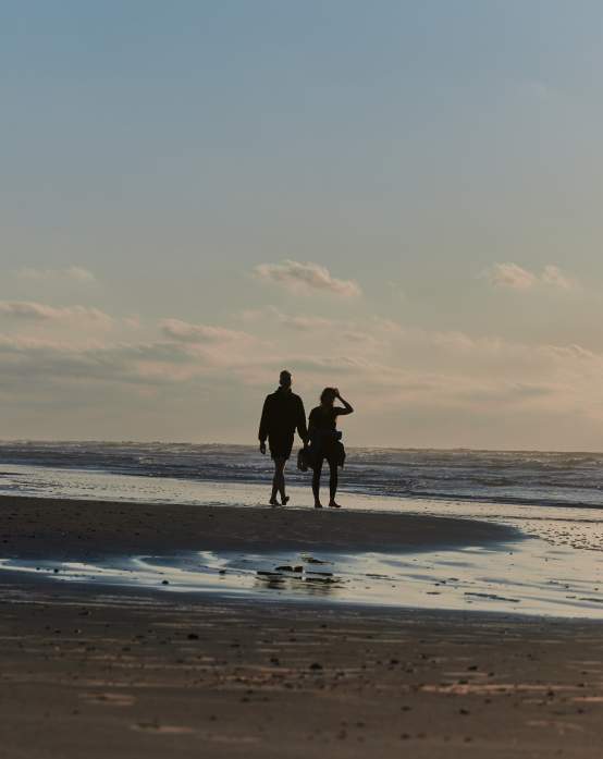 A silhouetted couple walks along the beach