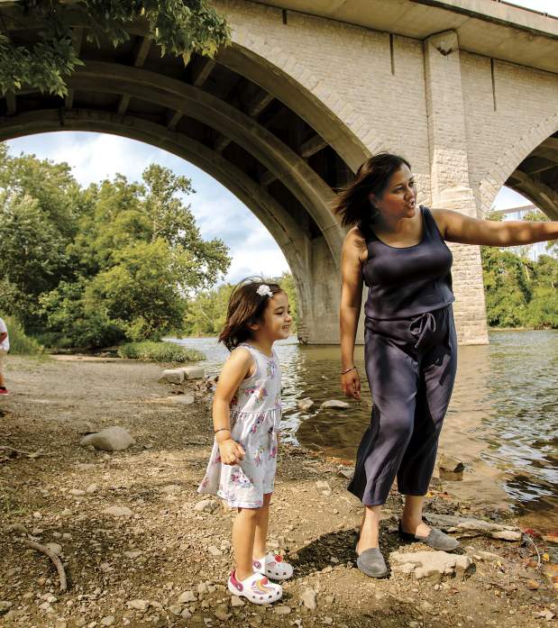 Woman and child explore the riverbank under a stone arch bridge at Dublin Springs Park on a sunny day.