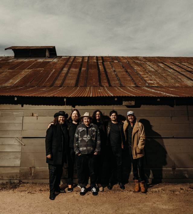 Uncle Lucius' 6-piece band poses in front of a rusted barn with dark skies.