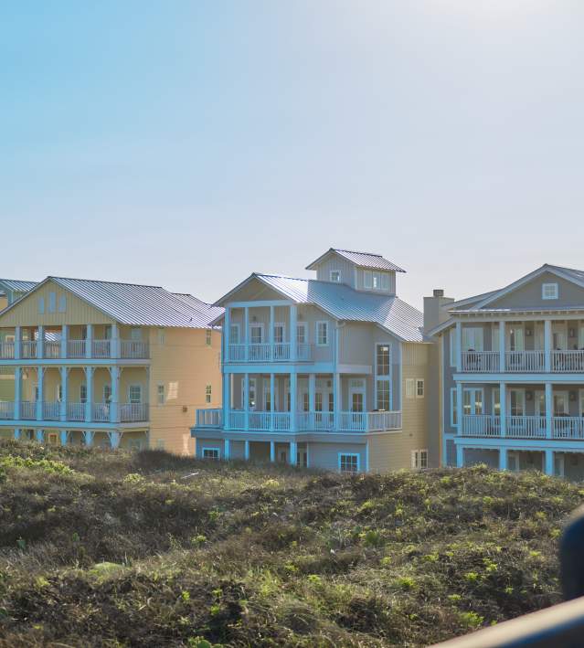 row of 4 large beach houses nestled in dunes in bright sunlight
