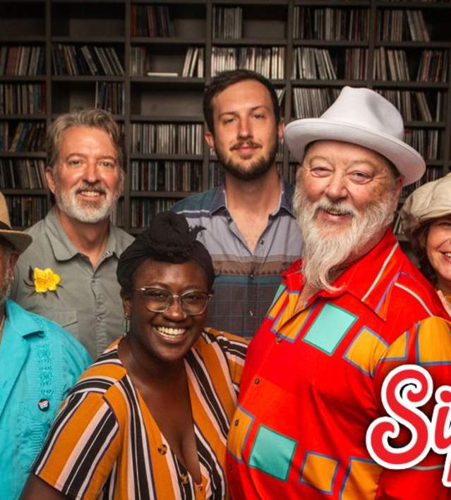 9-piece band poses in front of a bookshelf full of records