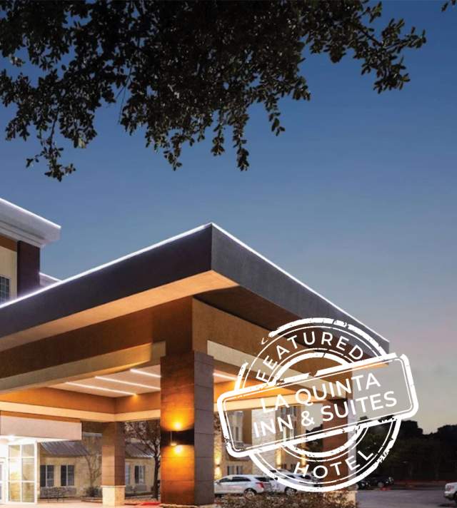 Exterior view of the La Quinta Inn & Suites by Wyndham Austin in Cedar Park, Texas, at dusk, showcasing the illuminated entrance drive, main tower, and bright brand signage.