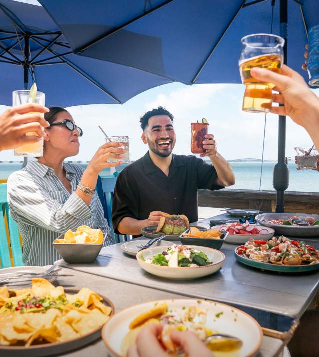 Friends enjoying seafood and cocktails at a waterfront restaurant on South Padre Island, Texas with views of the Laguna Madre Bay