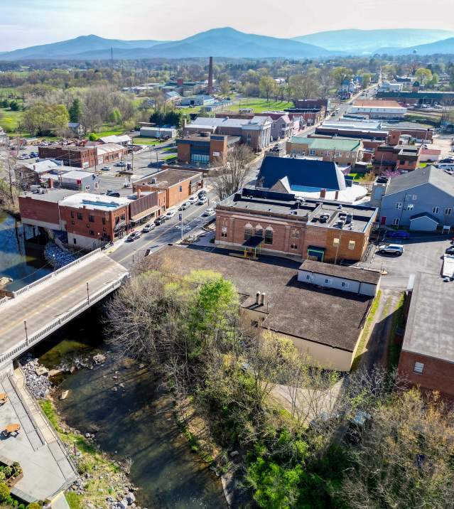 Aerial view of Downtown Luray in Page County, VA showing the river, tree‑lined streets, and surrounding mountains on a sunny day.