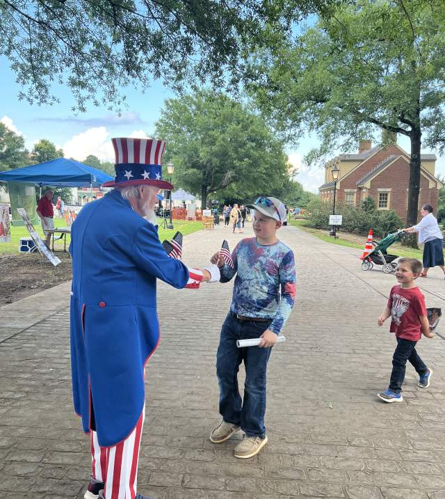 A man dressed as Uncle Sam hands a young boy an American Flag.