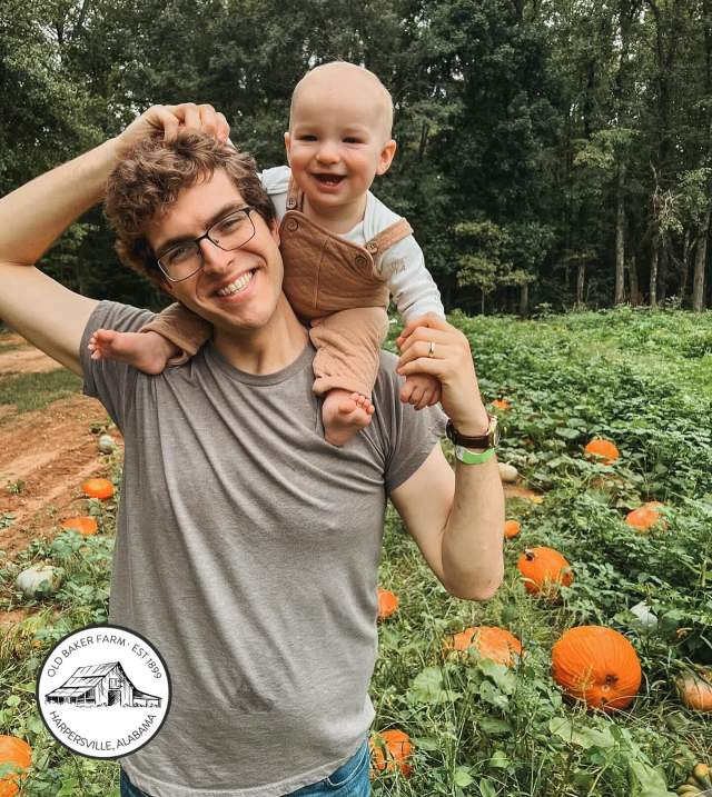 A dad smiles with a baby on his shoulders at Old Baker Farm Pumpkin Patch in Helena.
