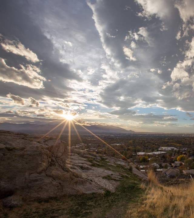 View of the Salt Lake Valley from the south with the sun shining.  Grass and boulder in the foreground, mountains in the background