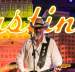 Ray Benson wearing a cowboy hat and holding his guitar on stage in front of a neon sign reading "Austin".