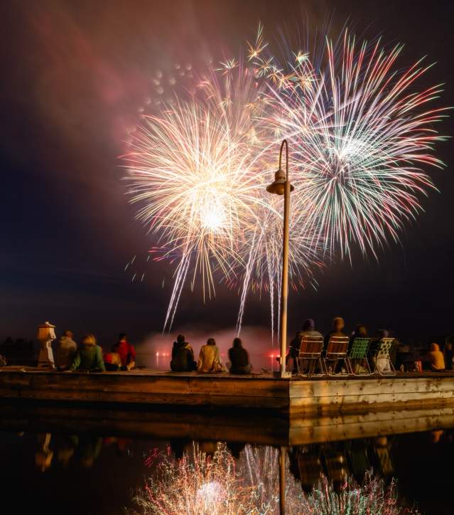 Fireworks explode over spectators watching at a dock