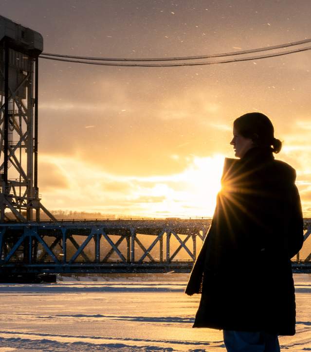 a person is silhouetted against a winter landscape and a lift bridge by the setting sun