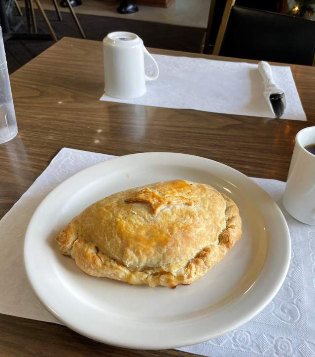 A pasty on a plate next to a cup of coffee