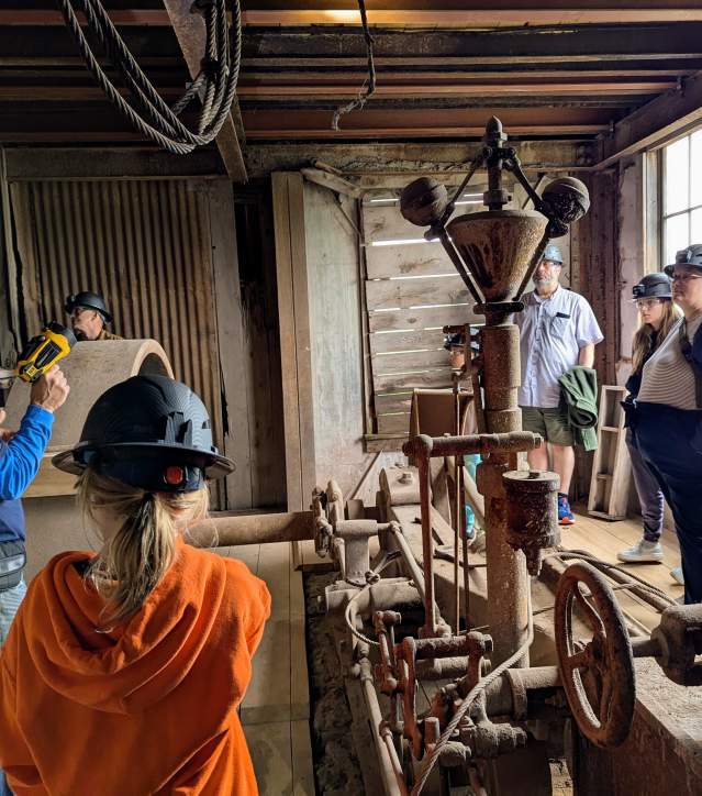 a tour guide leads a group of people in hardhats through a preserved copper mine building