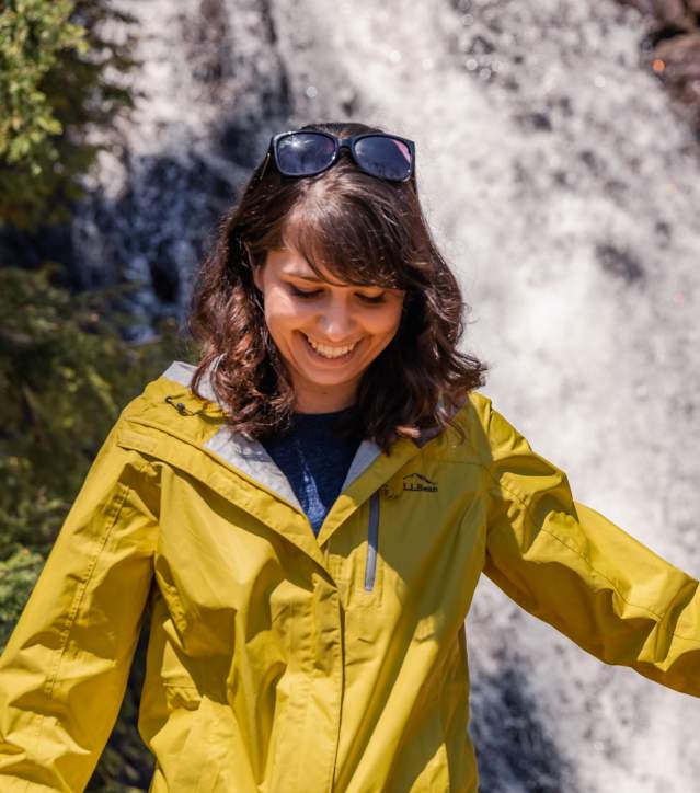 Woman with yellow coat in front of waterfall