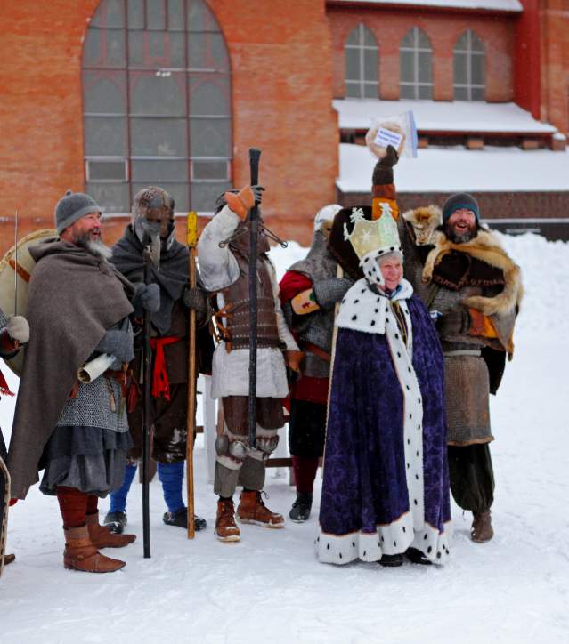 a group of people in medieval costume and a crowned figure cheer in the snow