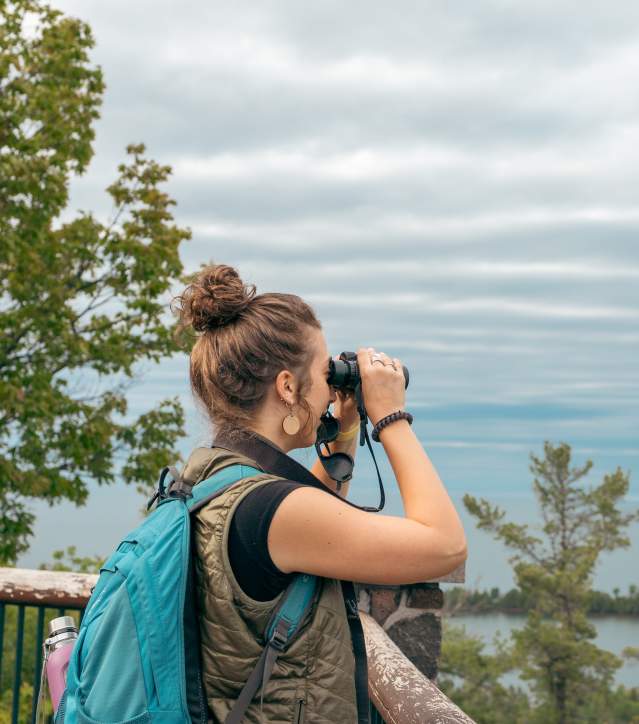 a figure looks through binoculars across a cliffside vita
