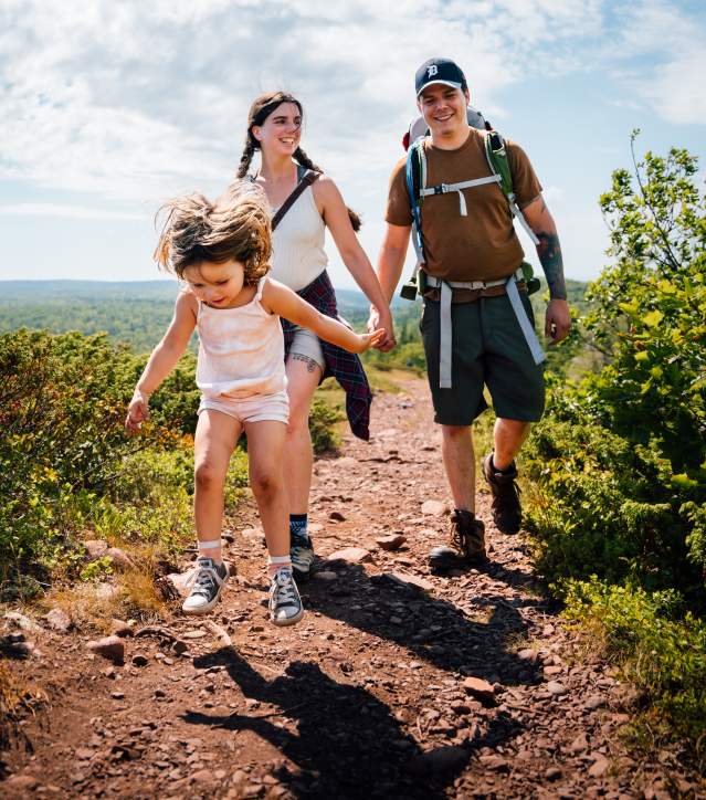 A young girl leaping in front of mom and dad while hiking