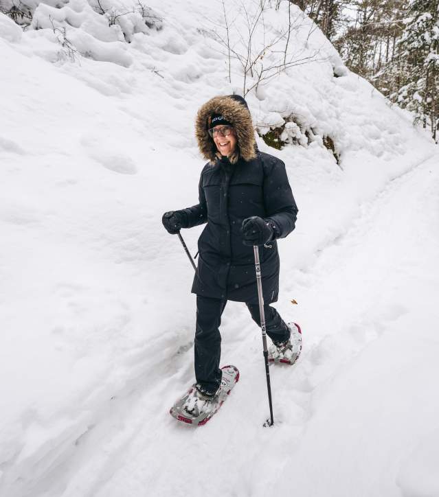 a person smiles as they use ski poles to snowshoe through a winter forest