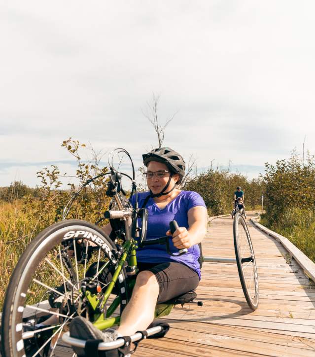 a person uses an adaptive bicycle to cruise a nature boardwalk