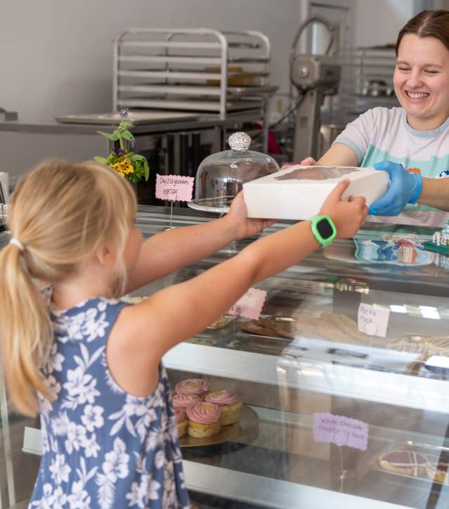 a person behind a bakery counter hands off a box of pastry to a young person