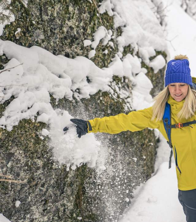 Woman brushes snow off boulder while snowshoeing