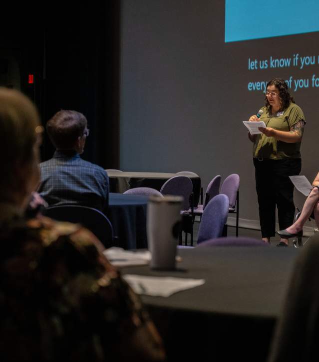 two presenters address a crowd, one standing and one utilizing a wheelchair