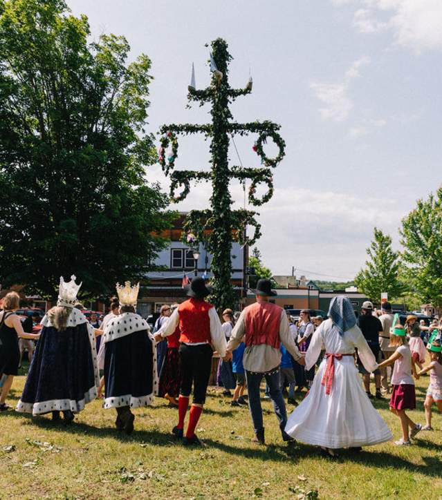 people in folk dress and costume circle dance around a midsummer pole