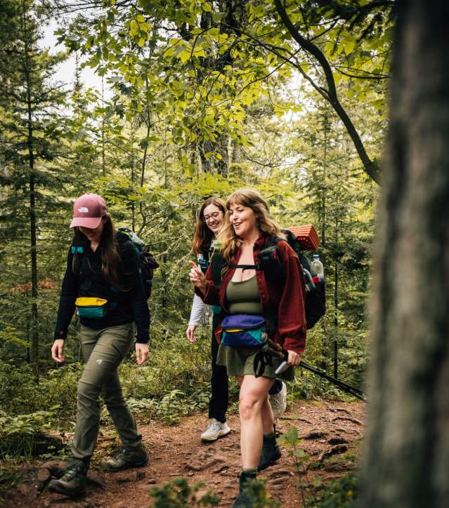 three figures in backpacking gear walk on wooded trail