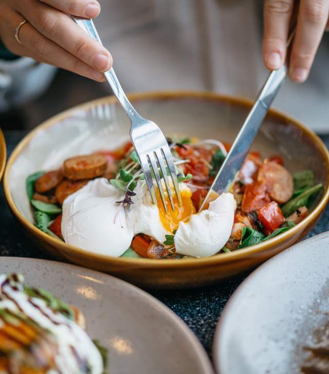 This is an image of a chef cutting into a poached egg on top of a breakfast platter.