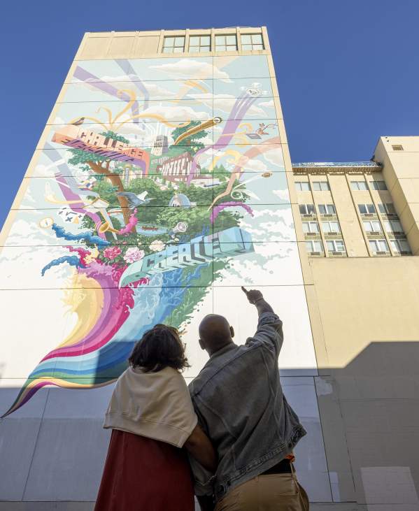 Couple pointing upward at tall, colorful mural
