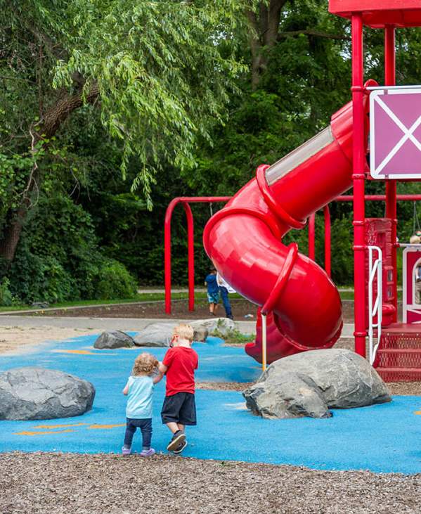 Two small children holding hands walking towards large red play structure