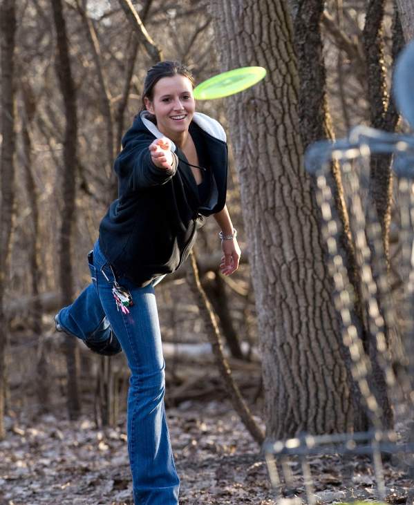 Woman throwing a bright green frisbee at a goal in the foreground