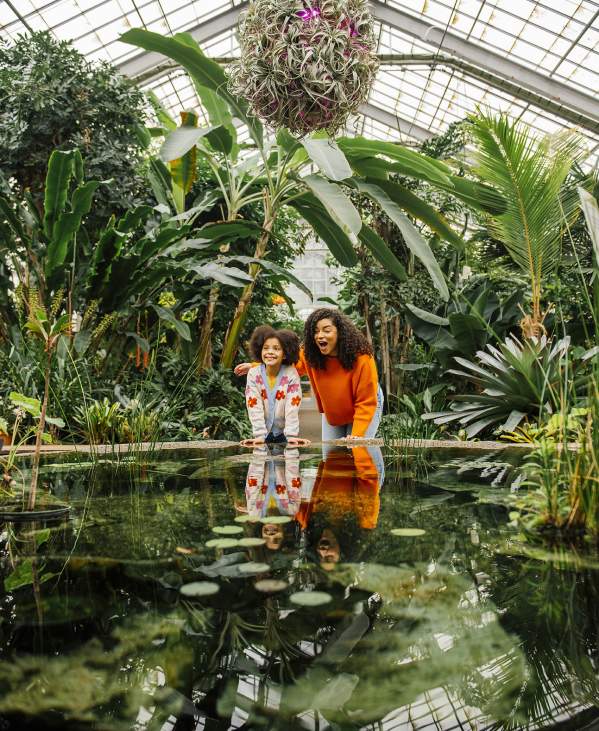 Little girl and woman looking at an indoor lily pond at the botanical gardens
