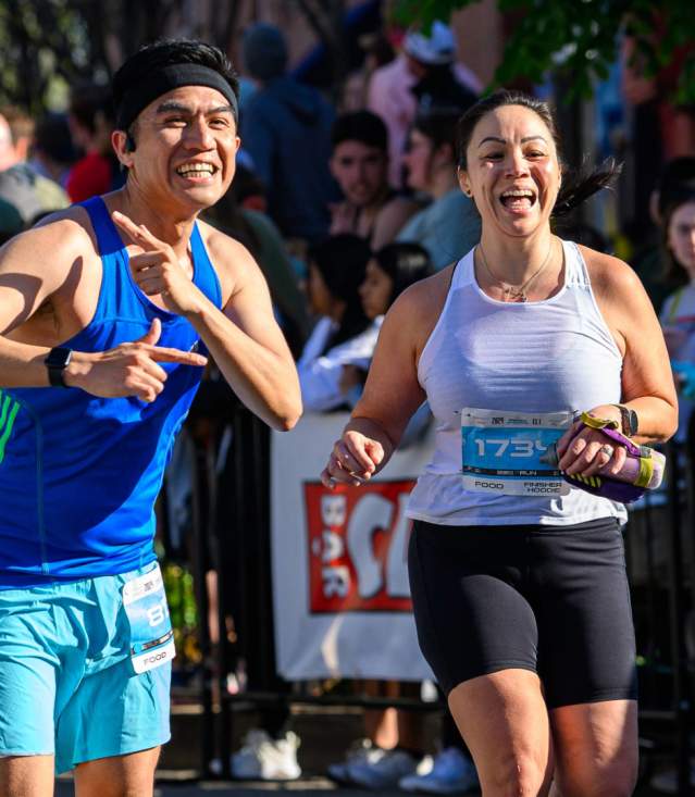 Two runners celebrate near the finish line of the Run Bentonville Half Marathon as cheering crowds look on.
