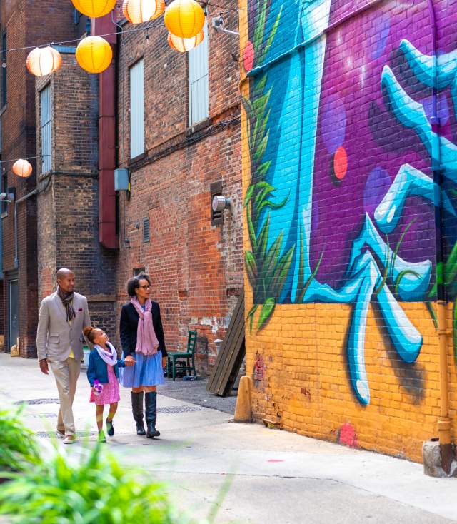 Father, mother, and daughter walking past a mural and the Porch off Calhoun in downtown Fort Wayne, Indiana.