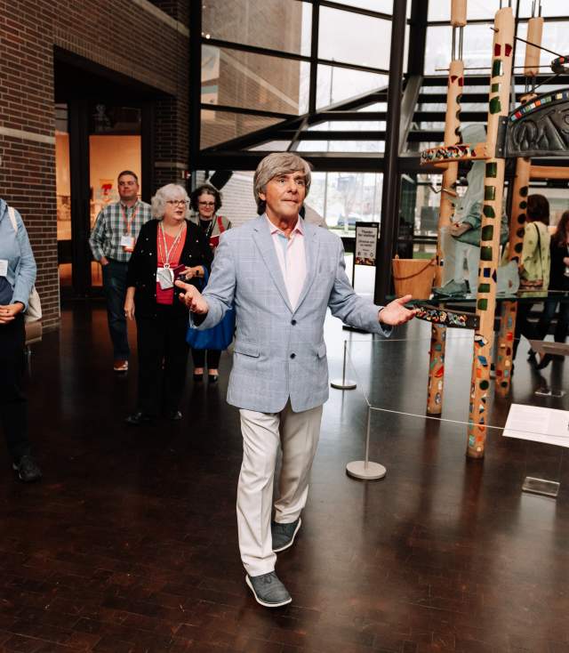 Charles Shepard of the Fort Wayne Museum of Art talking with travel journalists in the museum lobby with an art sculpture behind him,