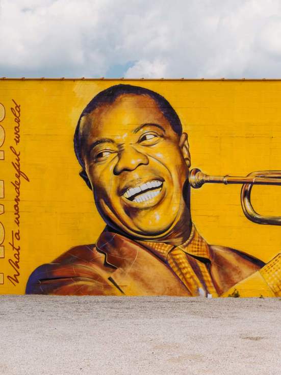Photorealistic, bright yellow mural of Louis Armstrong smiling and holding his trumpet up to play. The words "I love you" and "What a wonderful world" are painted on the left hand side of the mural.