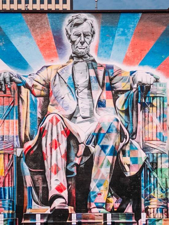 A large mural of Abe Lincoln sitting painted in brightly colored patterns primarily with red, blue, and white.
