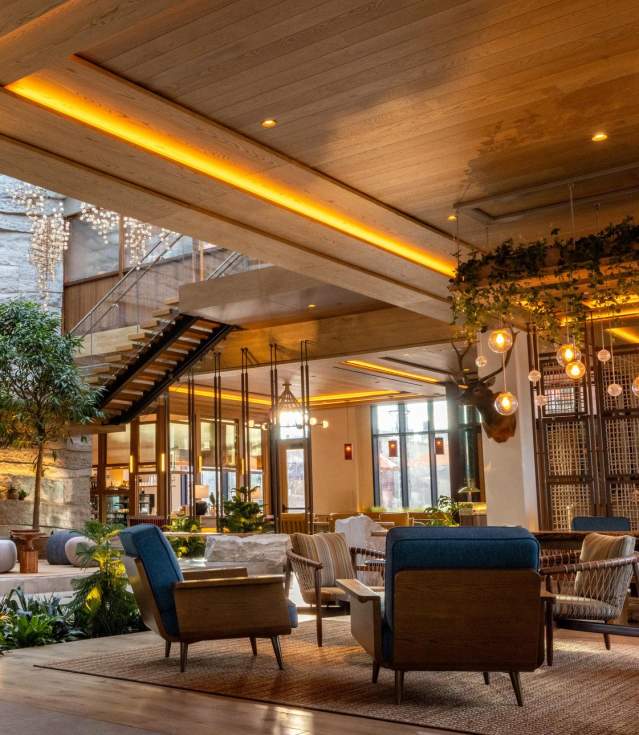 Modern lobby featuring natural stone walls, wooden beams, and stylish seating. Lush plants and warm lighting create a welcoming atmosphere.