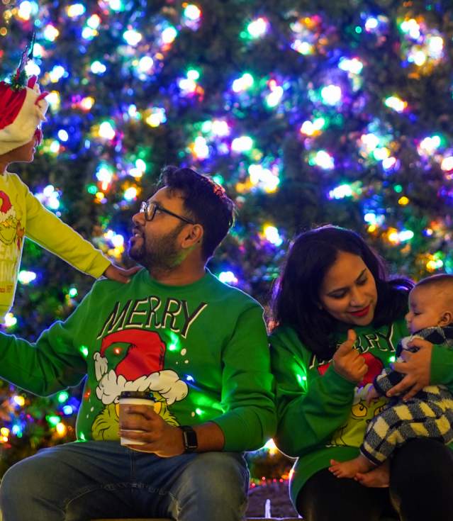 A family enjoys a festive evening by a brightly lit Christmas tree, surrounded by colorful holiday lights and decorations.