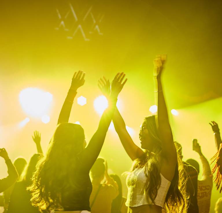 People dancing with their arms in the air in yellow light