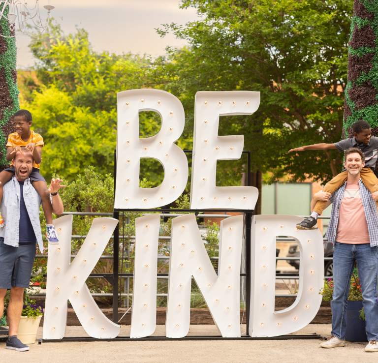 Family laughing in front of Be Kind sign at Elsewhere Garden Bar & Kitchen