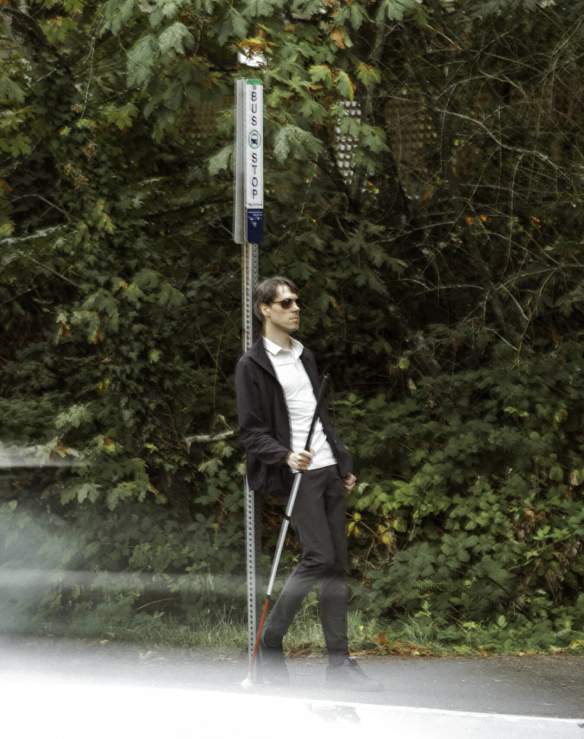 A blind man waiting at a bus stop.