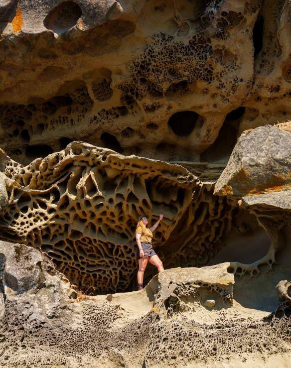 An individual stands against a wall of unique sandstone formations.